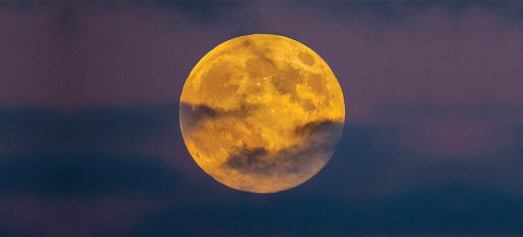 Super Full Moon captured in a golden color between a cloudy sky